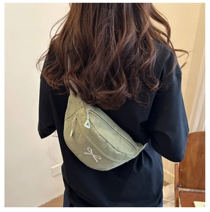 Detail view of a light green nylon crossbody bag featuring a white bow and zippers