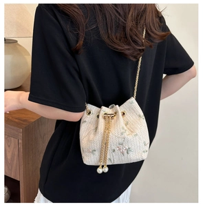 Detail of a straw bucket bag with floral embroidery and large pearl drawstring tassels