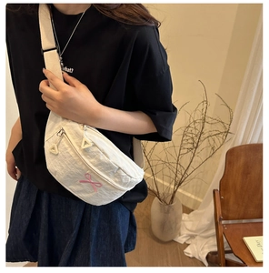 Close-up of white crossbody bag with pink ribbon embroidery and adjustable strap