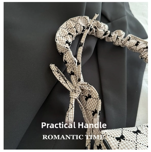 Close-up of beige plaid handbag featuring scrunchie style handle and black bow patterns