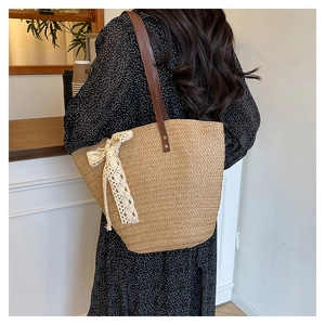 Detail of straw woven tote bag with beige lace bow and brown leather shoulder straps
