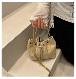 Detail of woven straw bucket bag with gold chain strap and pearl charm held by model