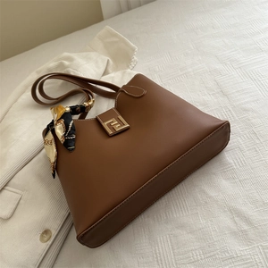 Brown leather large tote bag with gold metal logo and silk scarf on white suit background