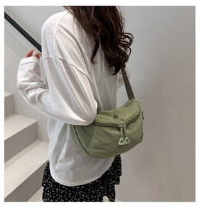 Detail view of a light green nylon crescent crossbody bag with double zip on a model