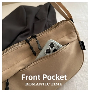 Detail of the front zipper pocket on a khaki canvas shoulder bag holding a smartphone