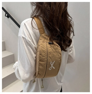 Close-up of light brown nylon crossbody bag with embroidery on a white staircase