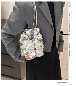 Detail of silver sequin bucket bag with metal chain strap worn on a gray suit jacket