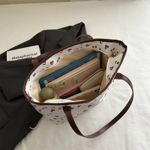 Large white tote bag with red cherry print and brown straps shown with daily essentials