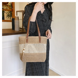 Detail of woven straw tote bag featuring brown leather handles and a tassel charm