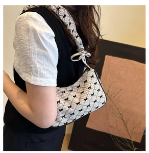 Detail of checkered hobo bag with black bows and ruffled strap on model's shoulder