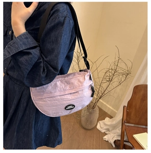 Close-up of light purple crescent bag with adjustable black strap and logo patch