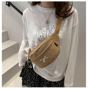 Detail of khaki nylon chest bag with white bow embroidery and adjustable strap