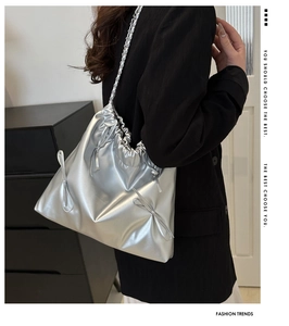 Detail of silver metallic tote bag with drawstring closure, bow decor and chain strap
