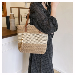 Detail of color-block straw tote with leather handles and decorative tassel ornament