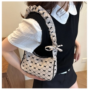 Close-up of beige plaid fabric bag featuring black bows and a pleated scrunchie strap