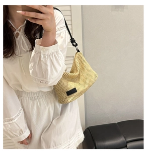 Detail of woven straw bag with black leather label and knotted strap shown in a mirror
