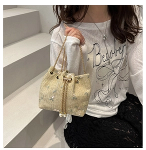 Detail of straw bucket bag with floral embroidery, chain strap and pearl drawstring