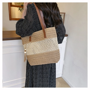 Detail of handwoven striped straw tote with leather handles and tassel on a model