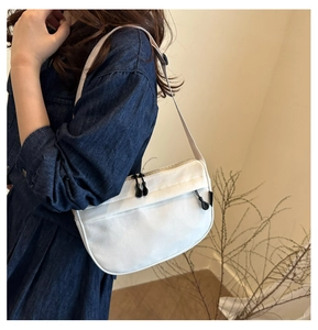 Close-up of a minimalist white crossbody bag with adjustable wide strap and zipper detail