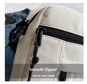 Close-up of a smooth black zipper and durable nylon fabric on an off-white crossbody bag