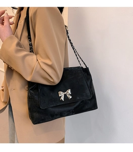 Close-up of black velvet shoulder bag with silver bow buckle and chain strap on a model
