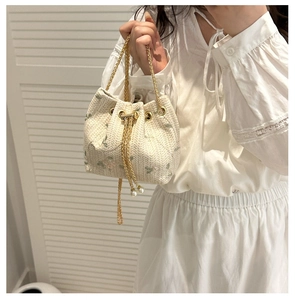 Detail of straw woven bucket bag with pearl pendant and gold chain strap in summer style