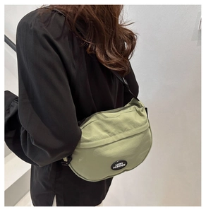 Detail view of the pale green dumpling bag with black brand patch and adjustable strap