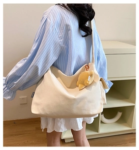 Detail of off-white canvas tote bag featuring a cute plush bear charm and black fashion tag
