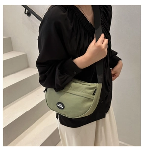 Close-up of light green half-moon crossbody bag with black Lucky Fashion logo patch