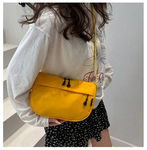 Close-up of bright yellow nylon crossbody bag with smooth black zippers and front pocket