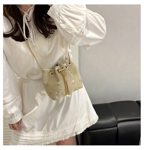Detail of straw bucket bag featuring pink floral embroidery and pearl drawstring