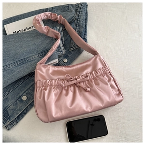 Détail d'un sac d'épaule en satin rose avec bandoulière plissée et nœud sur tissu blanc