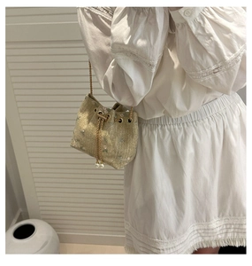 Close-up of mini straw bucket bag featuring floral embroidery and pearl chain drawstring