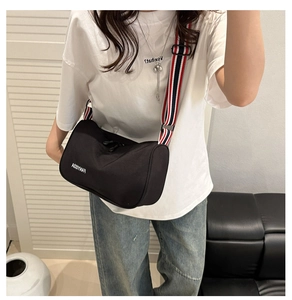 Model wearing black cylindrical crossbody bag with red and white striped shoulder strap