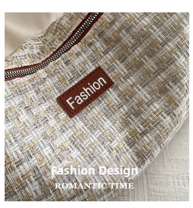Detail of tweed fabric texture and brown leather logo patch on a shoulder tote bag