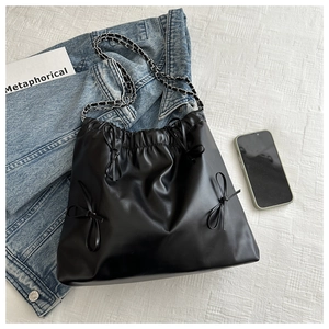 Detail of black leather drawstring bag with bow tie and silver-tone chain strap