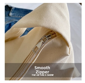 Detailed close-up of the smooth silver metal zipper on a cream canvas tote bag