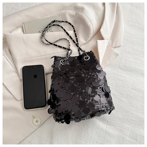 Detail of black sequin bucket bag with metal chain strap beside a smartphone for size reference