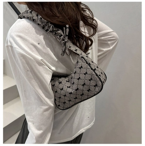 Detail of a black and white checkered shoulder bag with bow decor and ruffled cloud strap