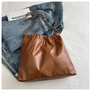 Detail of a brown leather chain bucket bag featuring a drawstring closure and soft texture