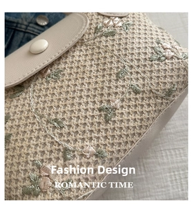 Detail of woven straw handbag featuring floral embroidery and beige leather flap closure
