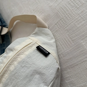 Sac bandoulière en nylon léger beige avec étiquette de marque et texture plissée