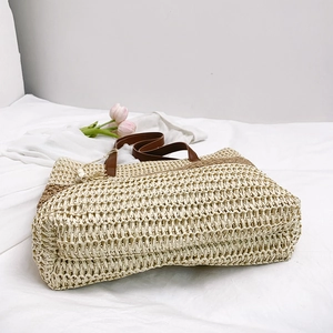 Beige straw tote bag with brown leather handles and side stripes for beach vacation