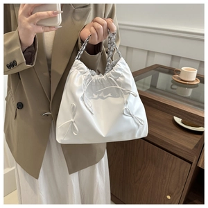Detail of white drawstring bucket bag featuring a side bow and silver metal chain strap