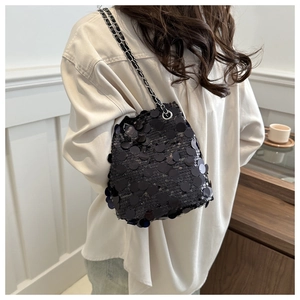 On-shoulder view of black sequined bucket bag with a silver chain strap for women