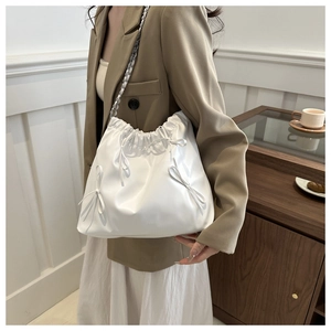 Detail of white drawstring bucket bag with bow decorations and chain shoulder strap