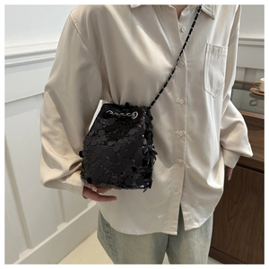 Detailed shot of black sequin bucket bag with leather chain strap on model in modern room