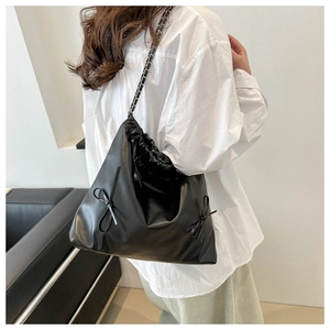 Model wearing black PU leather bucket bag with ribbon accents and metal chain strap