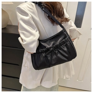Détail d'un sac à bandoulière noir plissé avec un nœud porté sur un blazer blanc