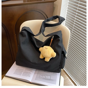 Close-up of black canvas hobo bag with star plush pendant on a chair in sunlight